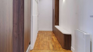 Un pasillo estrecho con suelo de madera, paredes blancas y un banco a lo largo de un lado.