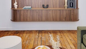 Una sala de estar moderna con un mueble de televisión de madera, un televisor de pantalla plana, una mesa de centro redonda con un bol de croissants y un sillón verde.