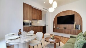 Una sala de estar moderna con una mesa de comedor redonda, sillas blancas, un sofá verde y un televisor de pantalla plana montado en una pared de madera.