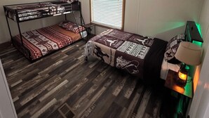 Een kleine kamer met twee stapelbedden, een raam met zonwering, een bureau met lamp en een radiator.