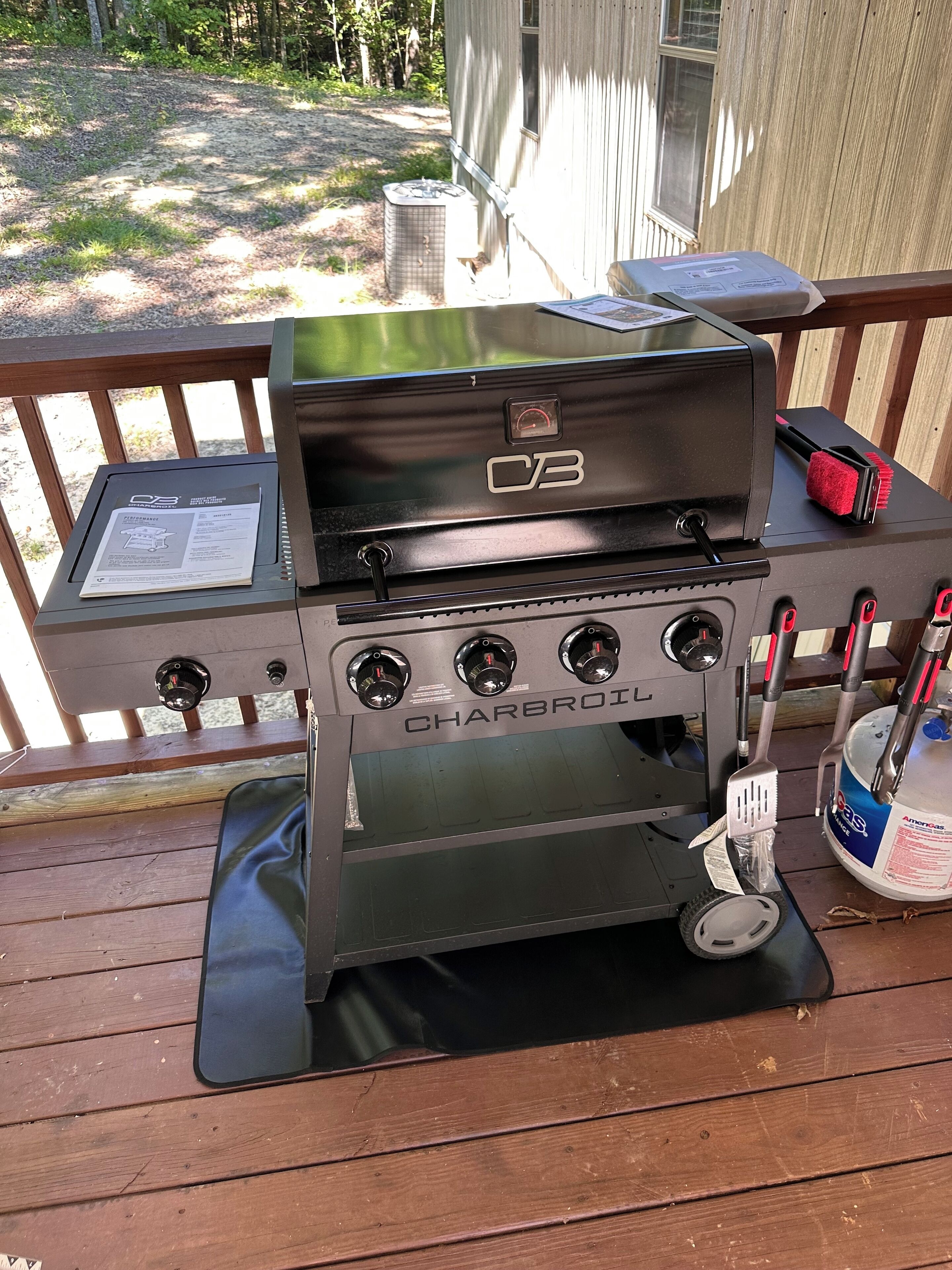Ein Charbroil Grill mit vier Brennern, einem digitalen Display und einer Propangasflasche auf einer Holzterrasse.