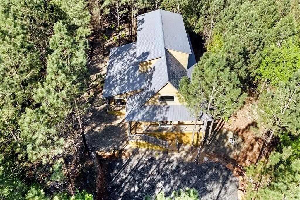 Une maison entourée d’une forêt dense, avec un toit en pente et un petit porche.