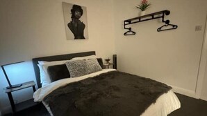 A bedroom with a bed, a nightstand, a wall-mounted shelf with a plant, and a picture on the wall.