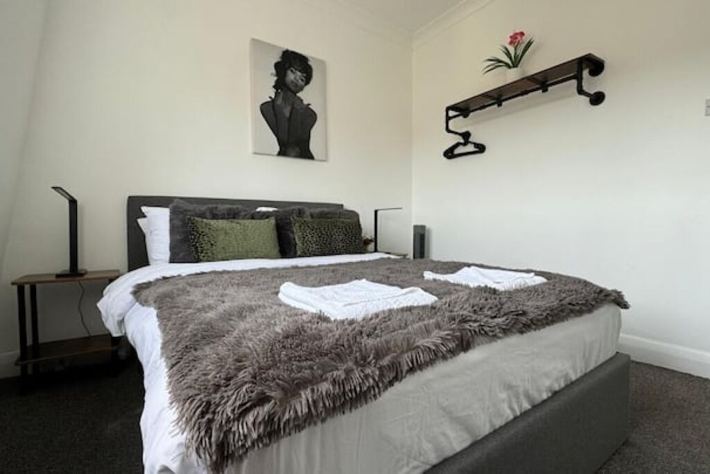 Une chambre à coucher avec un grand lit, une table de chevet, une étagère fixée au mur et un tableau encadré accroché au mur.