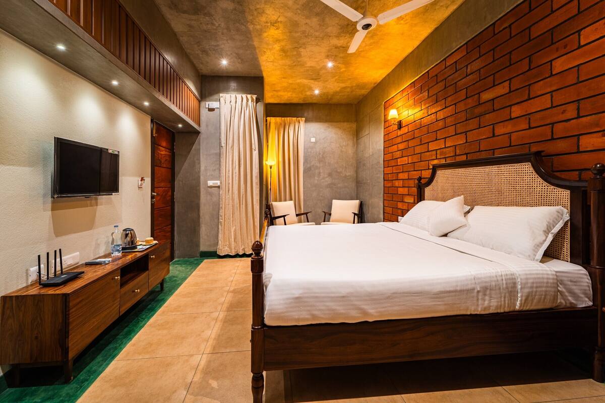 A bedroom with a wooden bed, a TV on a wooden console, a green carpet, and a brick wall.