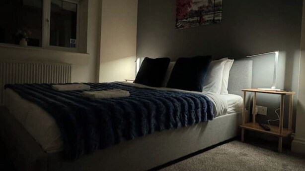 A bedroom with a bed, a bedside table, and a wall-mounted lamp.