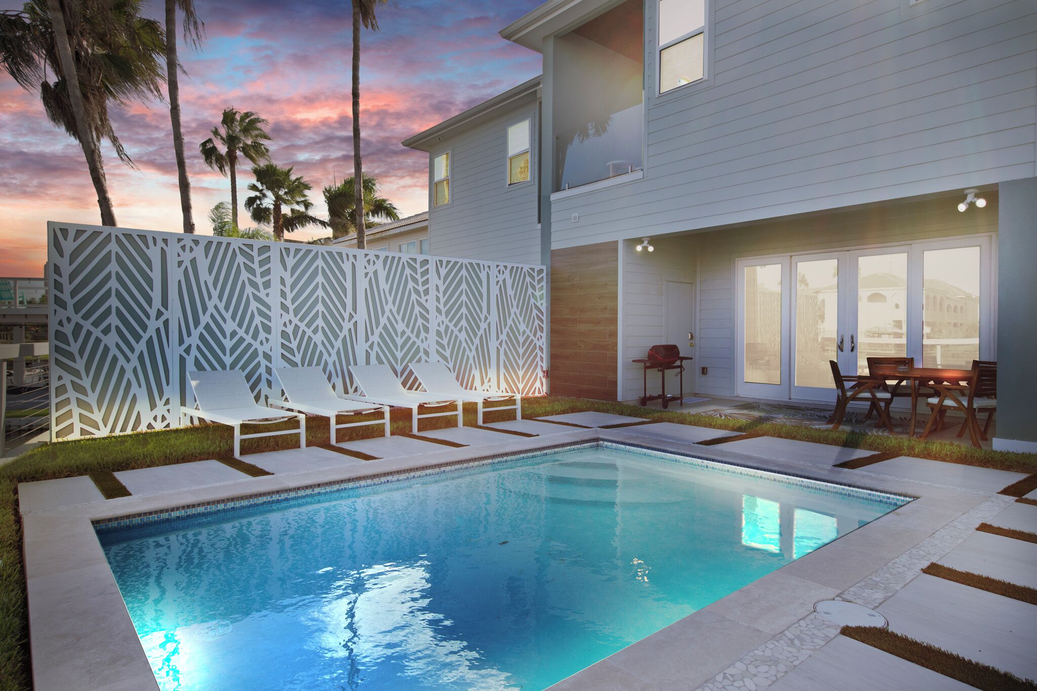 A modern pool area with a clear pool, white lounge chairs, and a decorative fence.