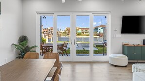 A spacious room with a large dining table, wicker chairs, a ceiling fan, and a view of a waterfront with buildings.