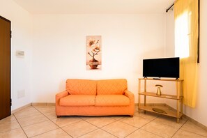 A living room with a sofa, a television on a stand, and a painting on the wall.