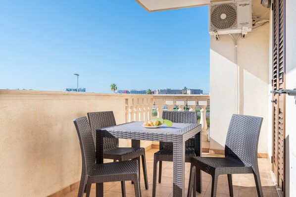 A balcony with a table and chairs, an air conditioning unit, and a view of the cityscape.