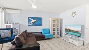 Uma sala de estar com sofá, poltrona azul, televisão e um armário.