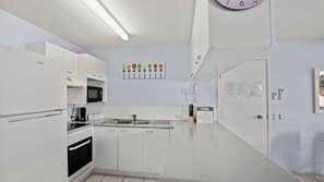 A modern kitchen with white cabinetry, a microwave, a sink, and a clock on the wall. - Lindomare Unit 3, 11 Orvieto Tce, Kings Beach (Kings Beach)