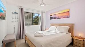 Quarto com cama, mesa de cabeceira, cortinas na janela, ventilador de teto e um quadro na parede.