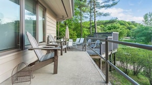 A balcony with outdoor seating, a view of a forest, and a building with large windows.