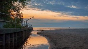 A beach with a wooden walkway leading to the water, a metal railing, and a cloudy sky.