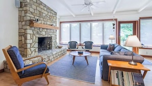 A living room with a stone fireplace, two chairs, a sofa, a coffee table, and a bookshelf.