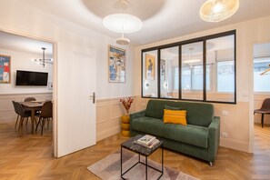 A modern living room with a green sofa, a coffee table, a TV, and a dining area with a wooden table and chairs.