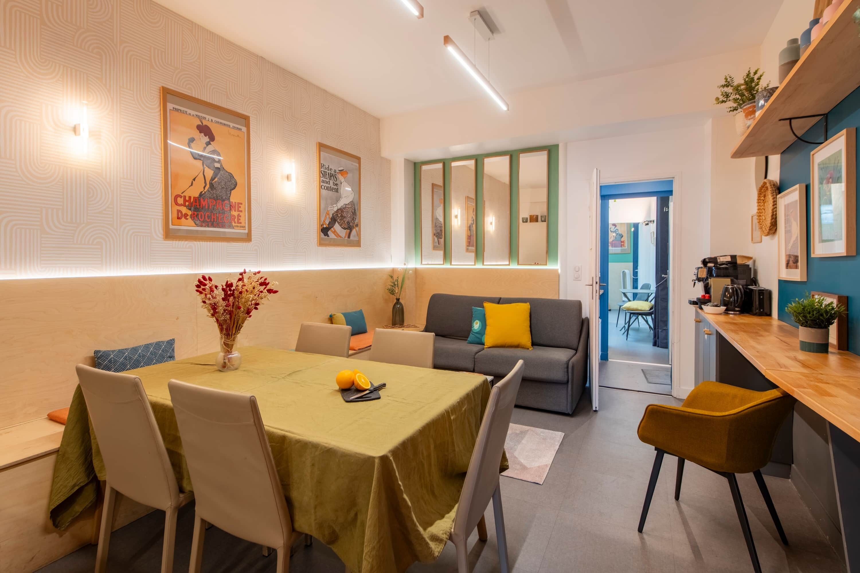 A modern dining area with a table set for two, a sofa, and a bar area.