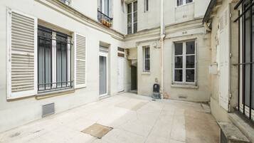 A courtyard with a tiled floor, white walls, and multiple windows with shutters.
