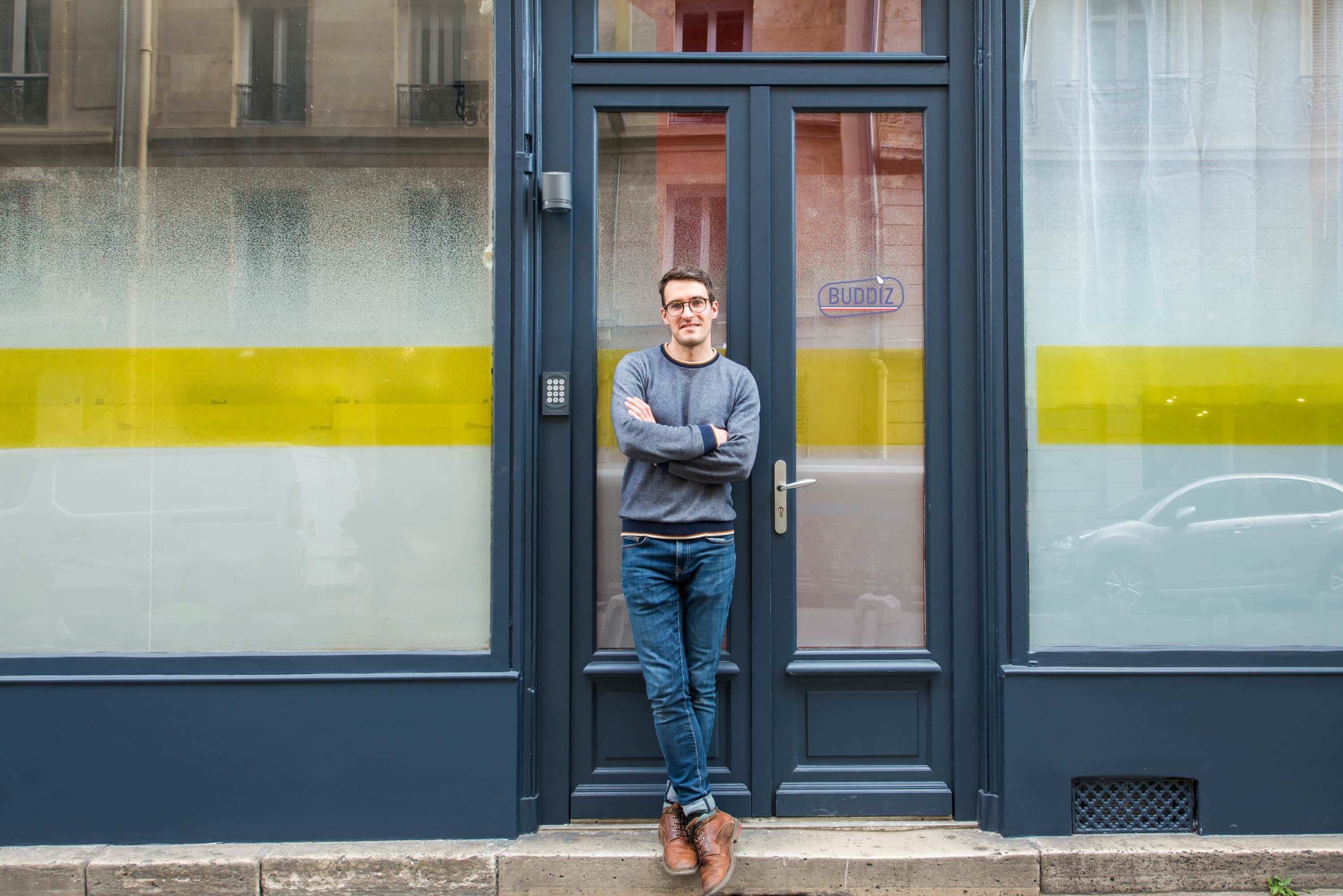 A person standing at the entrance of a building with a glass door and a sign that reads "BUDOZ".