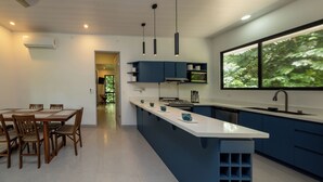 Una cocina moderna con una isla central, armarios azules, electrodomésticos de acero inoxidable y un amplio ventanal con vistas al verdor.