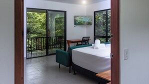 Habitación de hotel con cama, escritorio y silla. Tiene un balcón con vistas a zonas verdes.