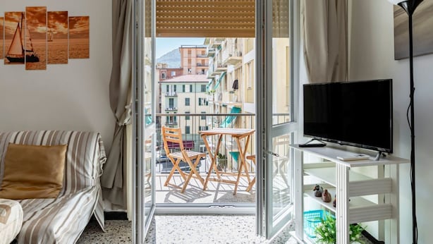 A balcony with a view of buildings, a sofa, a TV, and a lamp. - GuestHost - Cozy 75 sqm apartment, perfect for four people, located on the fourth floor of a building with an elevator (NOT wheelchair accessible).The property is located in a well-served residential neighborhood, just a short public transportation ride  (La Spezia)
