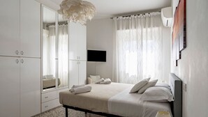 A bedroom with a bed, a mirror, a television, and a ceiling light. - GuestHost - Cozy 75 sqm apartment, perfect for four people, located on the fourth floor of a building with an elevator (NOT wheelchair accessible).The property is located in a well-served residential neighborhood, just a short public transportation ride  (La Spezia)
