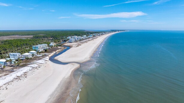 An aerial view of a coastal area with a long sandy beach, a clear blue ocean, and a row of buildings along the shore. - Papa's Palmetto Place (Port St. Joe)