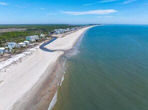 An aerial view of a coastal area with a long sandy beach, a clear blue ocean, and a row of buildings along the shore. - Papa's Palmetto Place (Port St. Joe)