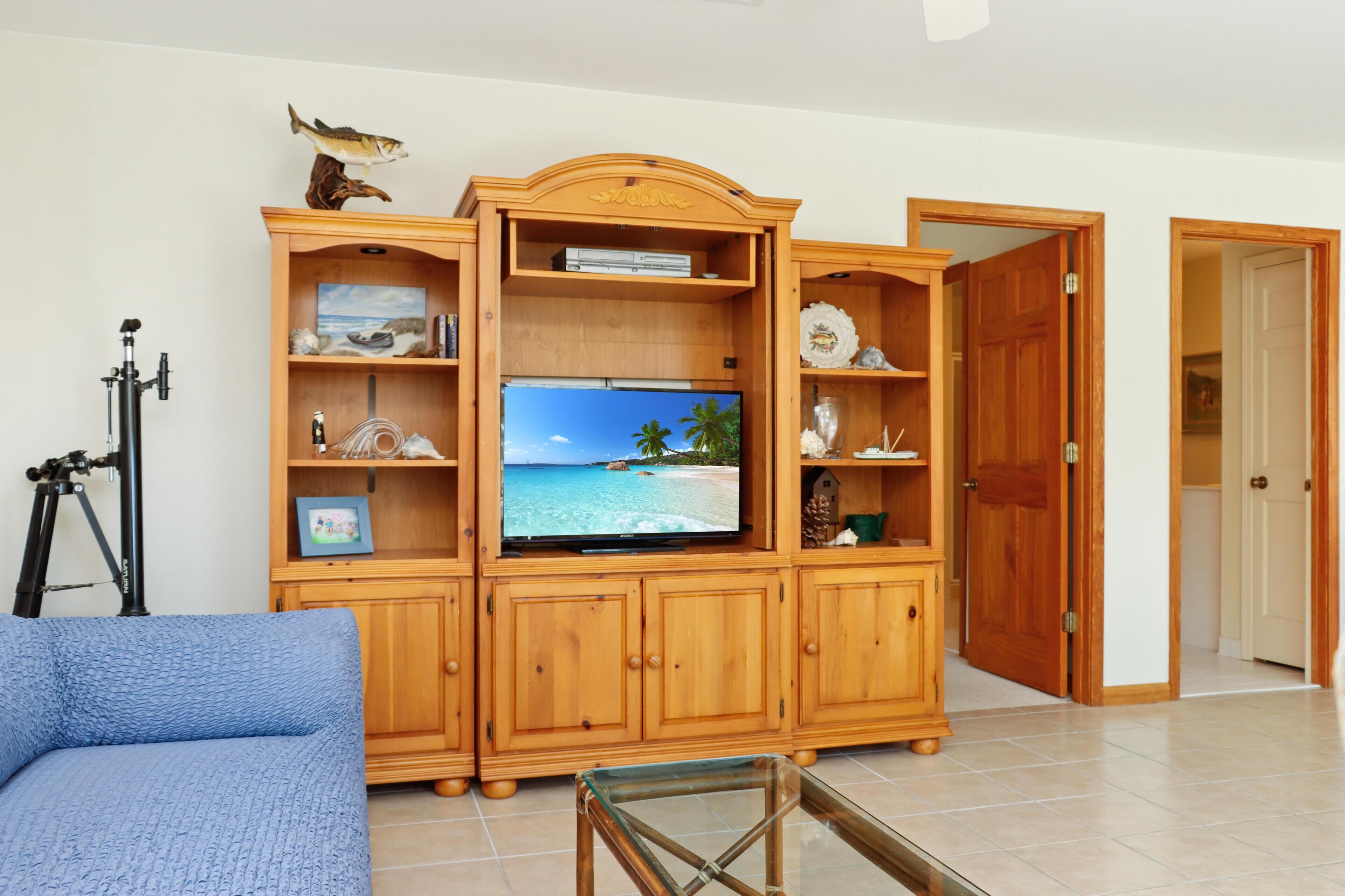 Een woonkamer met een houten tv-meubel, een televisie waarop een strand te zien is en een statief.