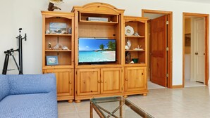 A living room with a wooden entertainment unit, a television displaying a beach scene, and a tripod. - Papa's Palmetto Place (Port St. Joe)