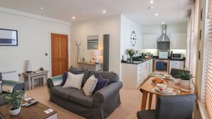 A modern living room with a sofa, a coffee table, and a dining area with a table set for two. A kitchen is visible in the background with modern appliances. - Jolly Roger (Whitby)