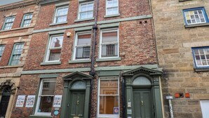 A multi-story brick building with green doors and windows, featuring a shop on the ground floor. - Jolly Roger (Whitby)