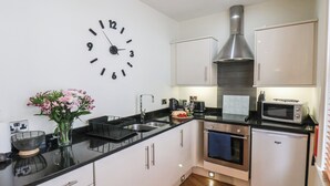 A modern kitchen with white cabinets, a black countertop, a stainless steel range hood, a microwave, and a built-in oven. - Jolly Roger (Whitby)