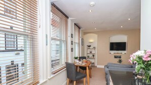 A dining area with a table set for two, a sofa, and a TV mounted on the wall. - Jolly Roger (Whitby)