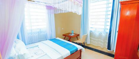 A hotel room with a bed, a desk, a chair, and a wardrobe.