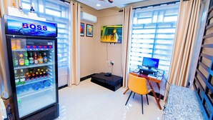 A hotel room with a minibar, a desk with a computer, and a large window with curtains. - HBE HOTEL KIGAMBONI (Dar es Salaam)
