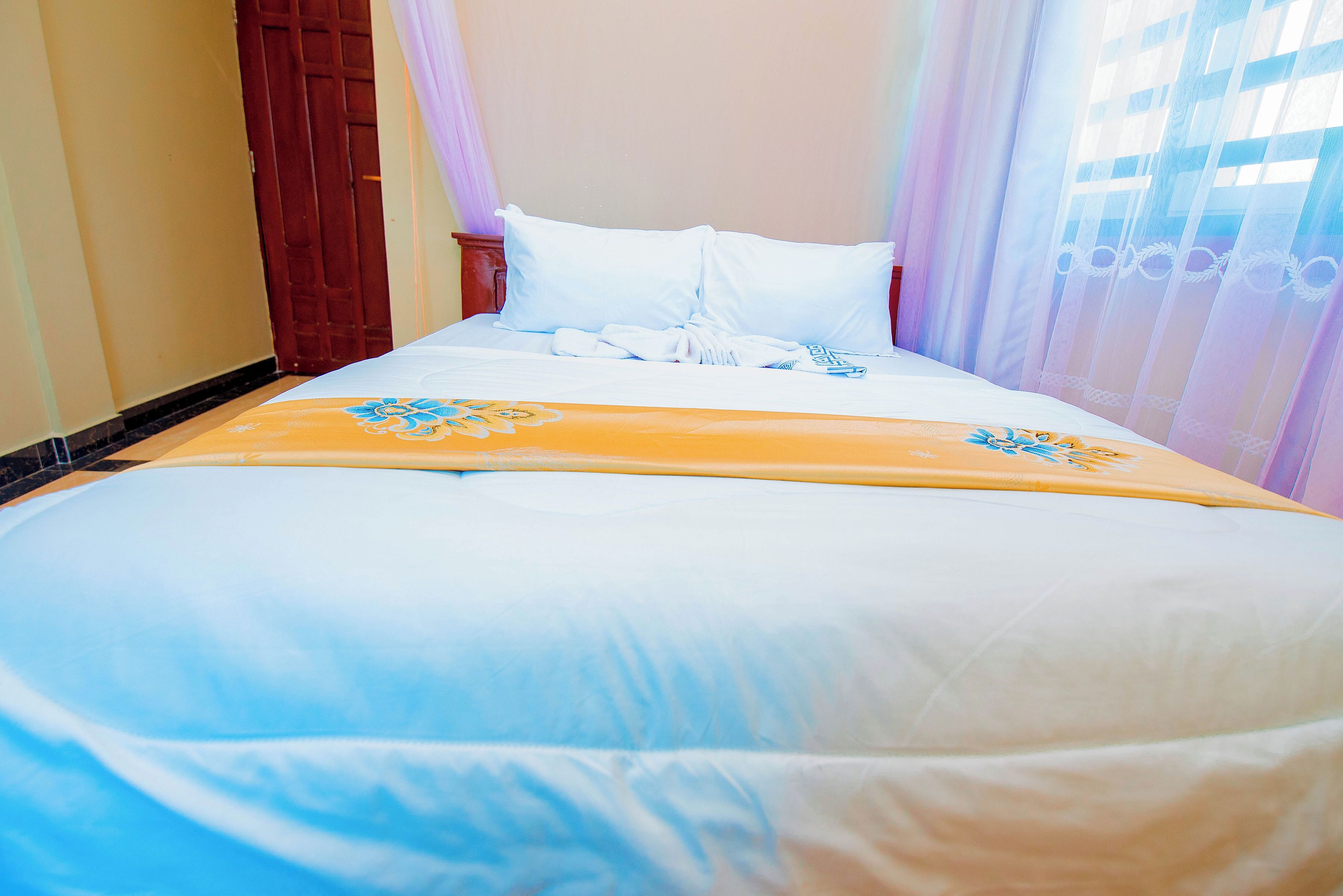 A neatly made bed with a white and blue bedspread, a yellow decorative runner, and white pillows.