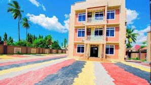 A multi-story building with a 'Welcome' sign, a balcony on the second floor, and a paved area with colorful patterns. - HBE HOTEL KIGAMBONI (Dar es Salaam)