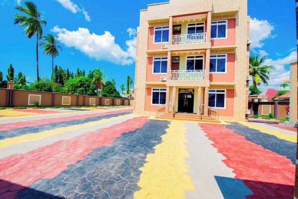 Um edifício de vários andares com uma placa de 'Welcome', uma varanda no segundo andar e uma área pavimentada com padrões coloridos.