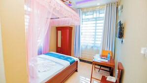 A neatly arranged hotel room with a bed, a desk, a chair, a wardrobe, and a television on the wall. - HBE HOTEL KIGAMBONI (Dar es Salaam)