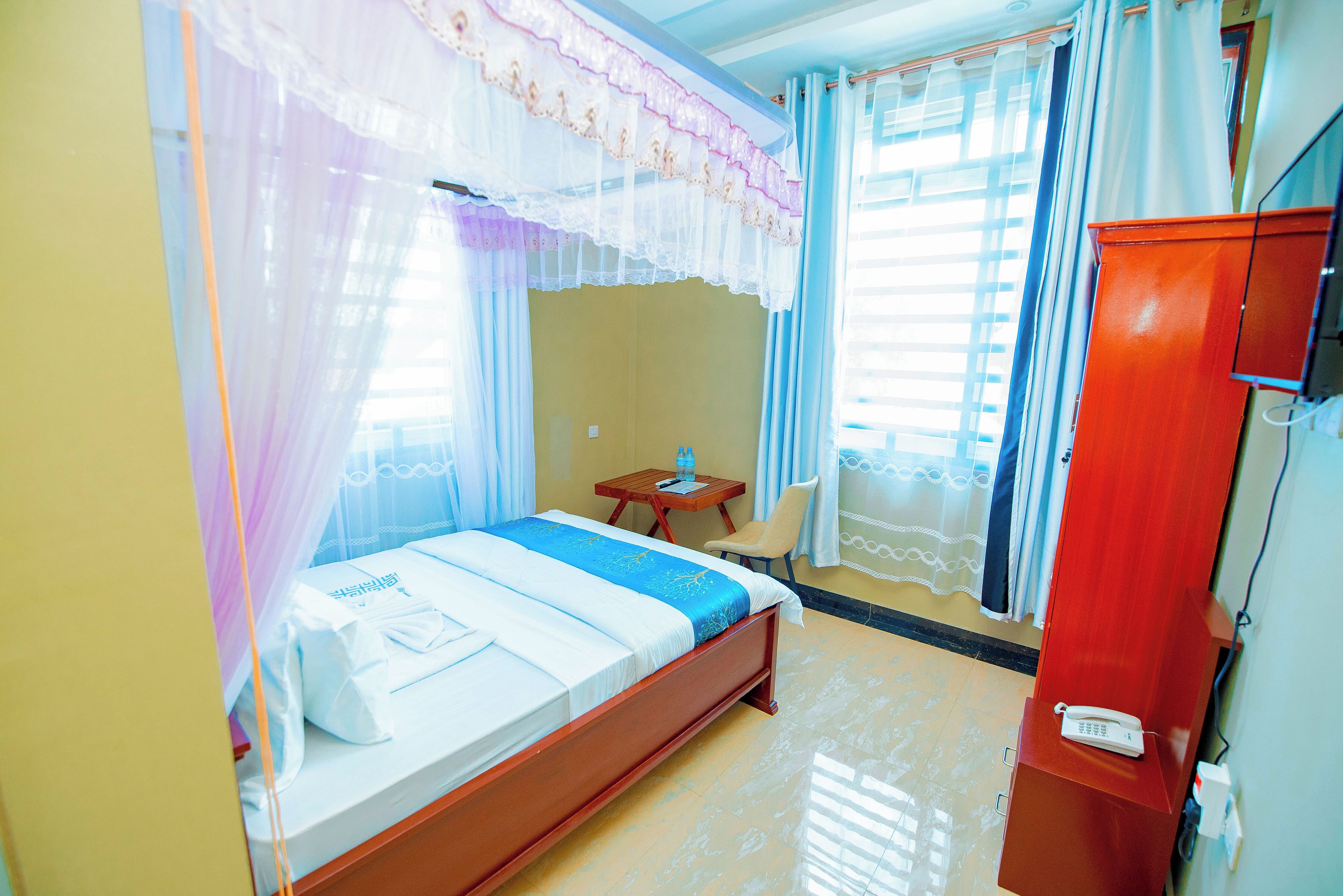 A hotel room with a bed, a wooden nightstand, a telephone, and a wardrobe.