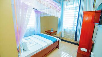 A hotel room with a bed, a wooden nightstand, a telephone, and a wardrobe.