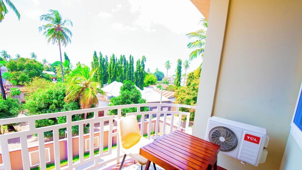 A balcony with a wooden table and a white chair, overlooking a lush garden with palm trees and other greenery. - HBE HOTEL KIGAMBONI (Dar es Salaam)