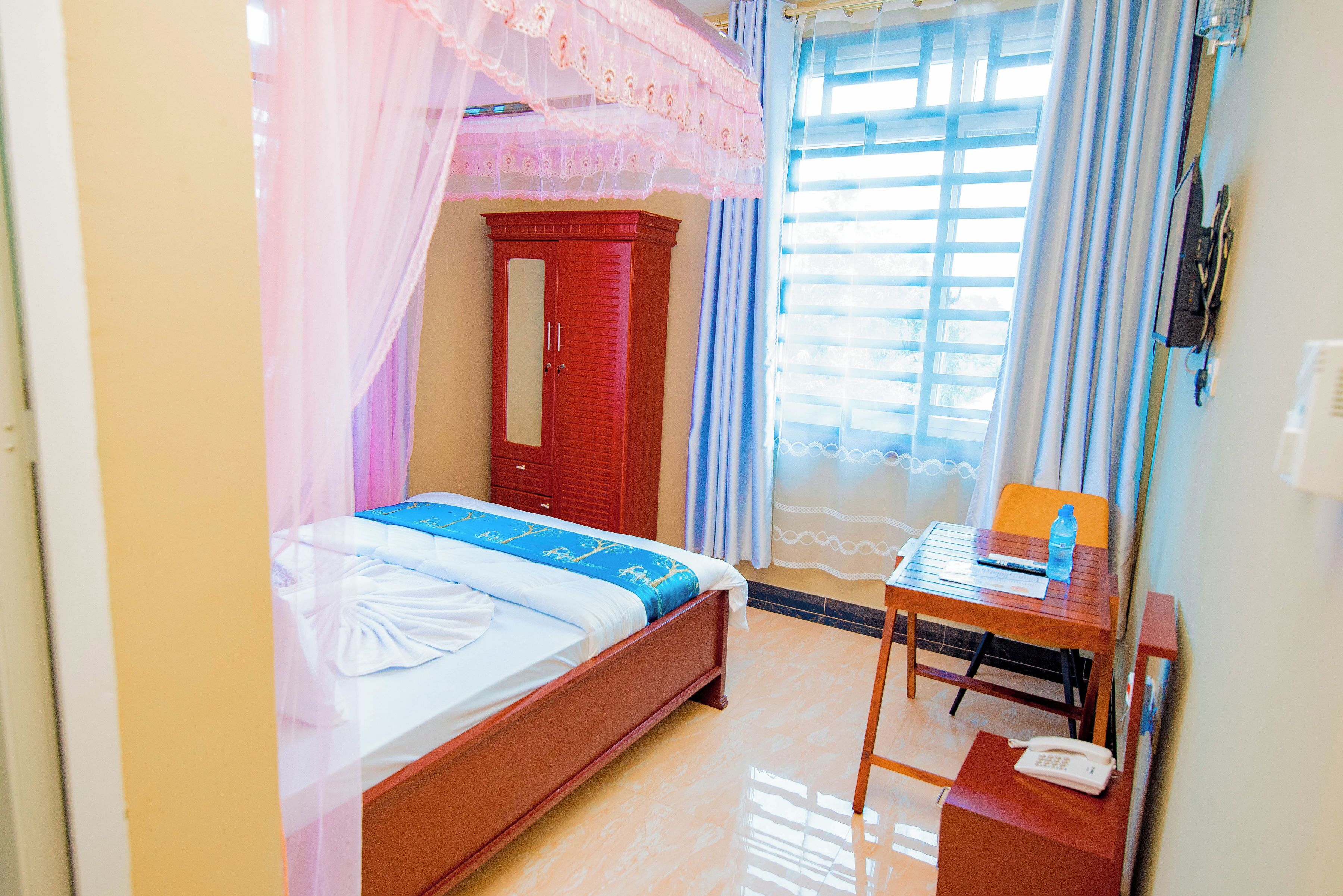 Une chambre à coucher avec un lit, une armoire en bois, un bureau avec une chaise et une fenêtre avec des rideaux.