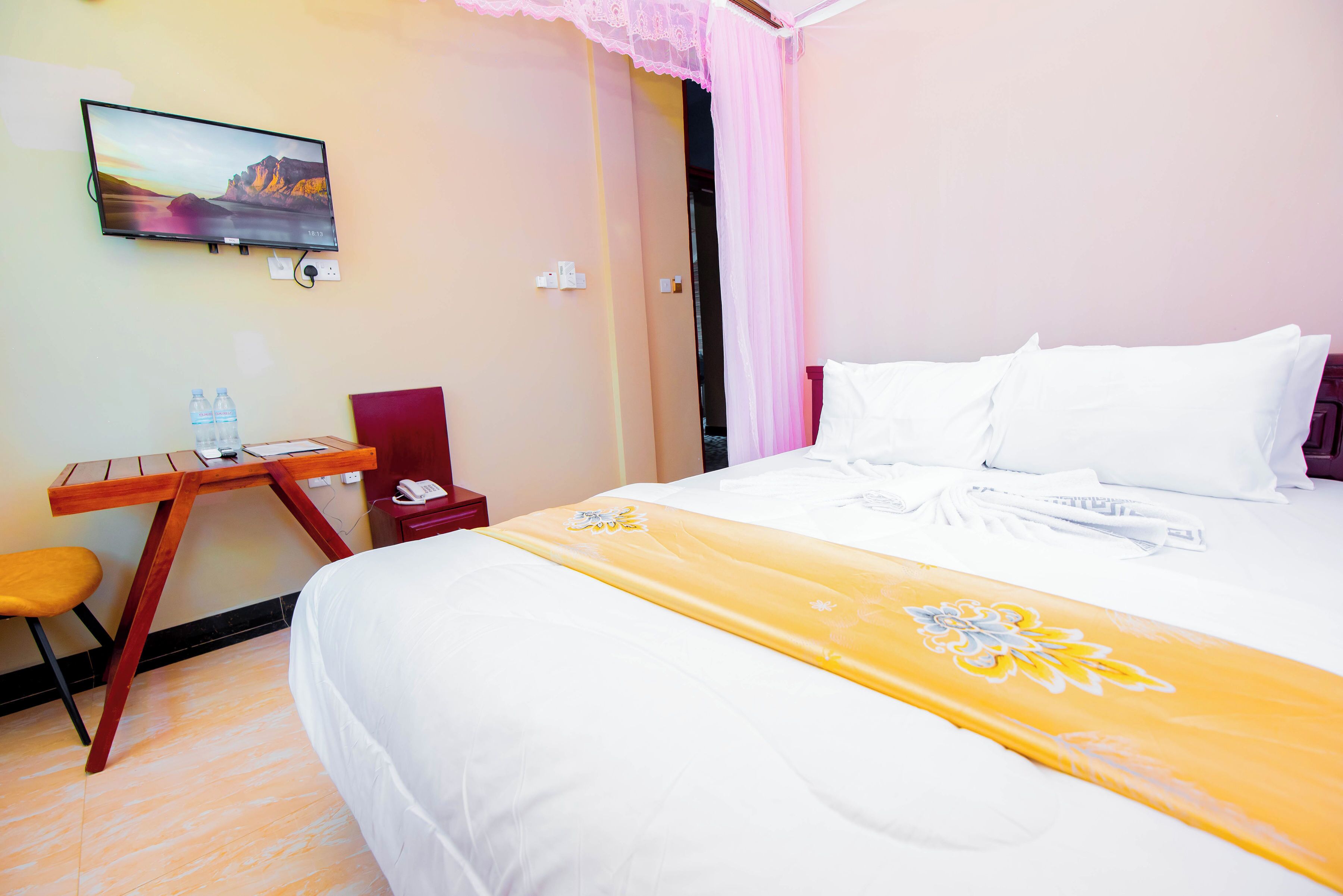 A hotel room with a bed, a desk with a chair, a television on the wall, and a window with curtains.