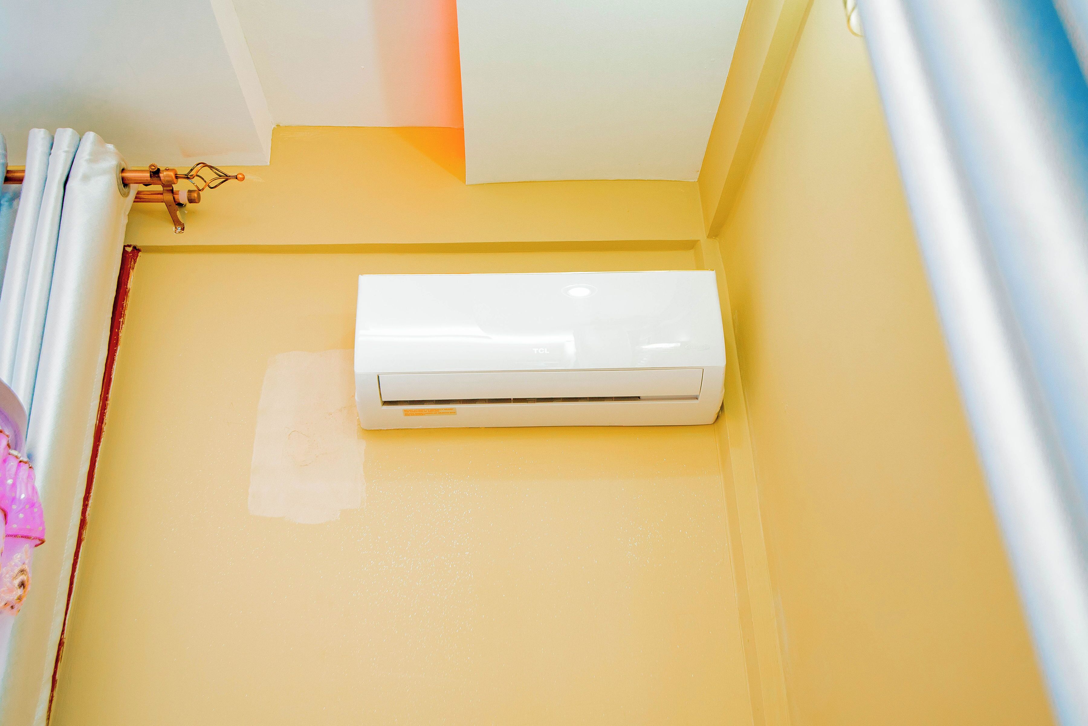A white air conditioning unit mounted on a yellow wall in a room.