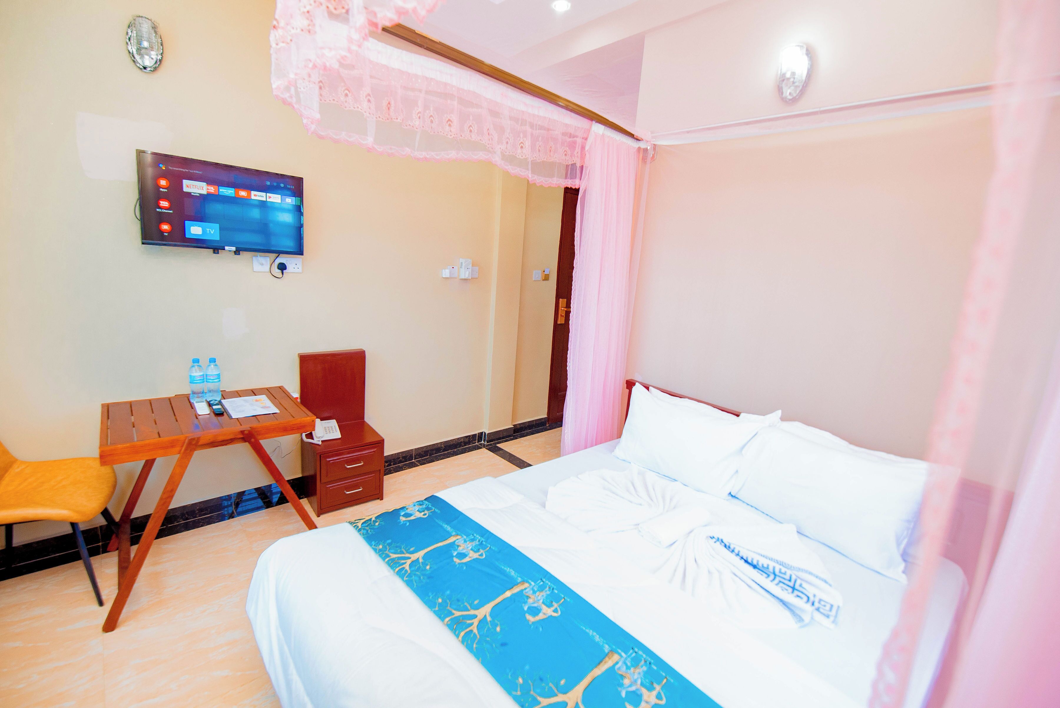 A hotel room with a bed, a desk, a chair, a TV, and a window with curtains.