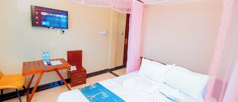 A hotel room with a bed, a desk, a chair, a TV, and a window with curtains.